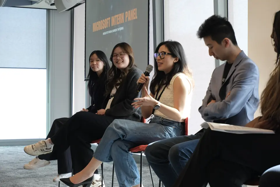 Four panellists on stools, one speaking into a microphone; the screen behind them reads Microsoft Intern Panel.
